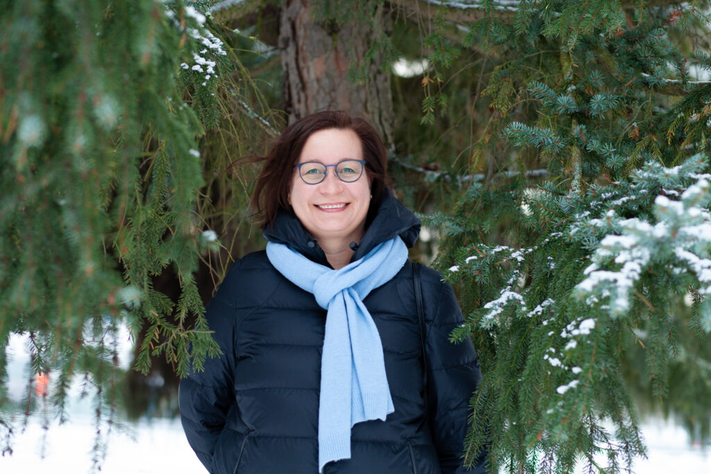 Tiina Koivisto seisoo lumisessa maisemassa kuusen edessä.