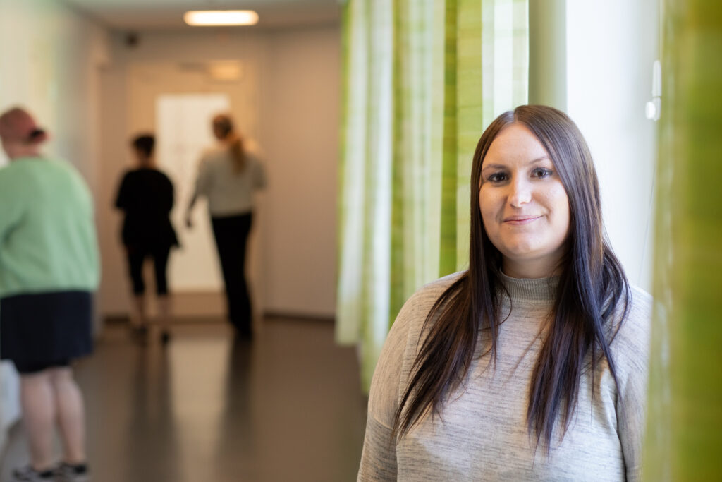 Henkilökuvassa Jessica Iso-Oja. Taustalla näkyy kolme henkilöä takaapäin.