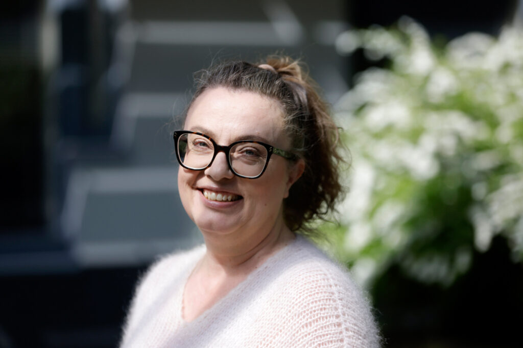Työterveyslaitoksen johtava tutkija Jenni Ervasti lähikuvassa katsoo kameraan ja hymyilee. Jenni on kuvattu ulkona.