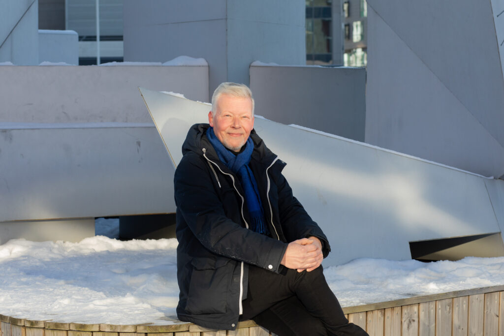 Henkilökuvassa professori Petri Nokelainen istuu ja takana näkyy lunta ja rakennusta.