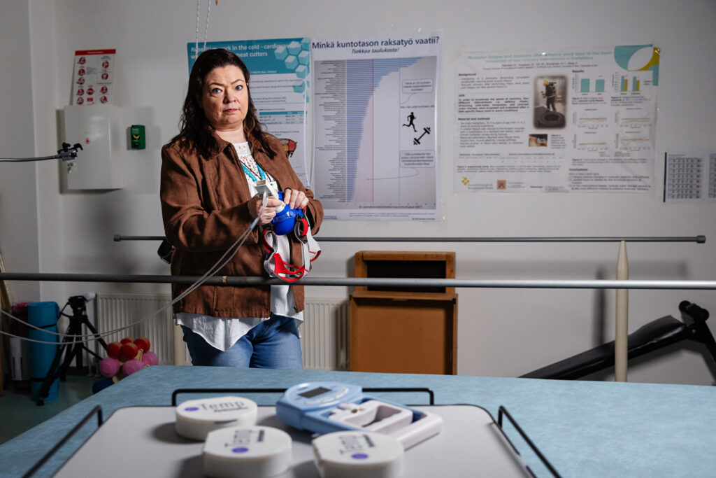 Työterveyslaitoksen (TTL) tutkija Jutta Karkulehto fysiologian laboratoriossa. Karkulehto pitää kädessään mittalaitetta.