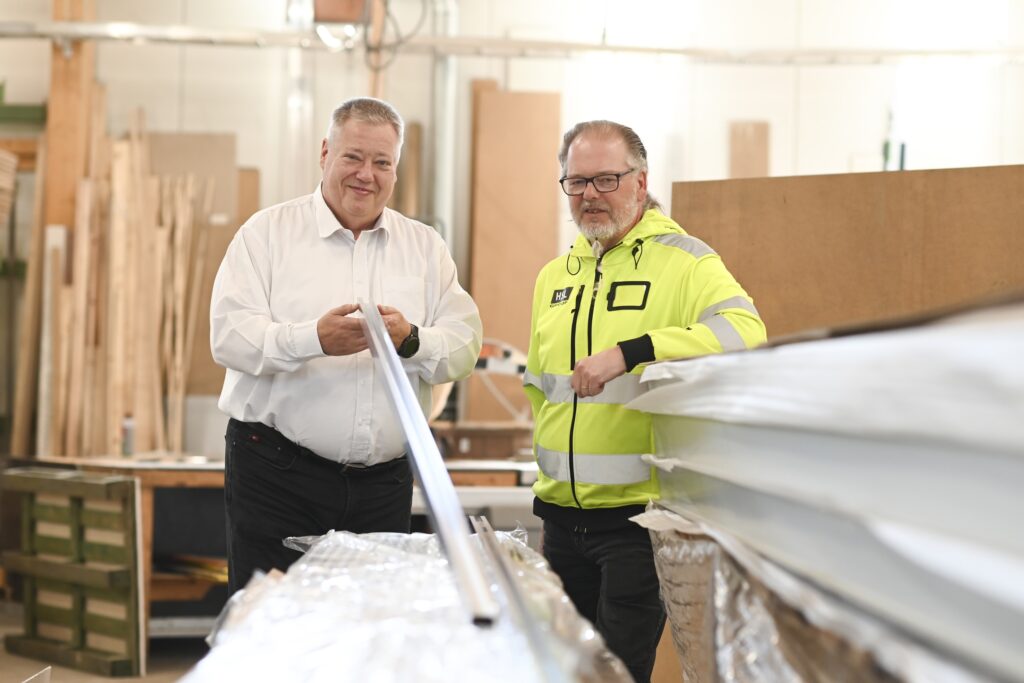 Panu Hämäri ja Mika Pentikäinen seisovat HSL Groupin tehdastiloissa ja Hmäri pitelee käsisään putken päätä. Taustalla näkyy tehtaan tiloja.