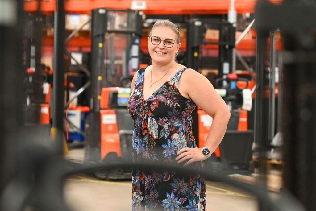 Jaana Kuivalainen seisoo Toyota Material Handling tiloissa ja taustalla näkyy trukkeja.